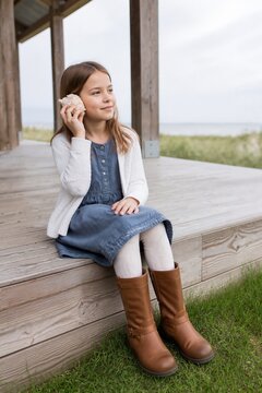 Girl listening to seashell outdoors by the beach