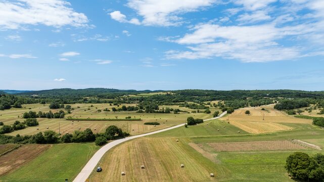 Aerial view of the rural landscape of Sterna, featuring rolling fields with hay bales, a winding road, and patches of trees under a blue sky in Sterna, Istarska zupanija, Croatia.