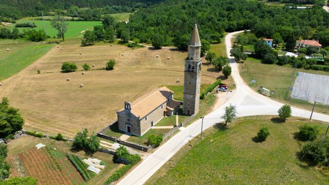 Aerial view of the historic Church of St. Vitalis with its tall stone bell tower, surrounded by rural fields and greenery in Sterna, Istarska zupanija, Croatia.