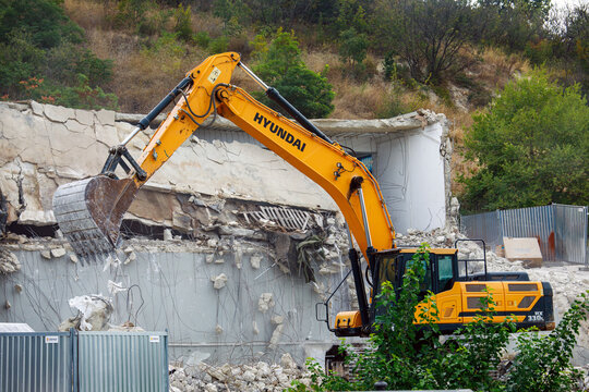 Varna. Bulgaria. 26.08.2026 A powerful yellow excavator demolishes a concrete office building, representing the concept of destruction and construction renewal. High quality photo