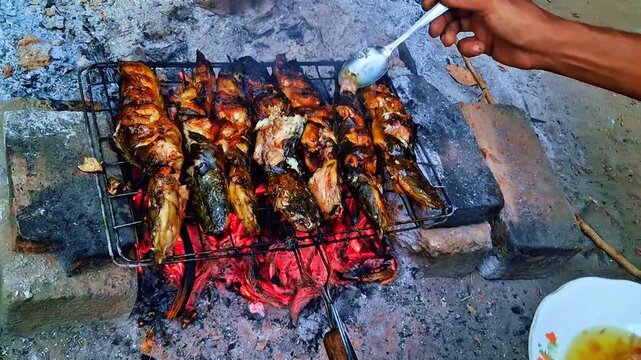Grilling and seasoning fresh catfish over glowing hot coals with traditional spices, creating a mouthwatering smoke aroma.
