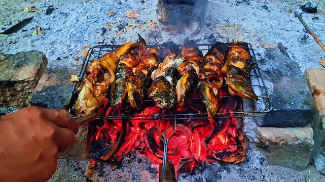 Close-up of perfectly grilled catfish smoking over red-hot burning coals, showcasing a rustic outdoor cooking scene.
