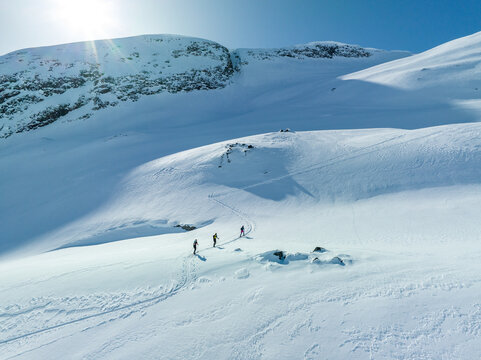 Aerial view of three people ski touring up the snow-covered slopes of Hogstolen mountain under a bright sun in Fjord, More og Romsdal, Norway.