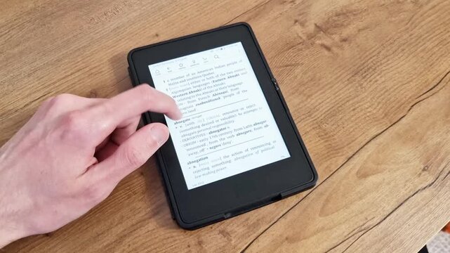 Hand holds electronic book reader with open page on wooden table surface