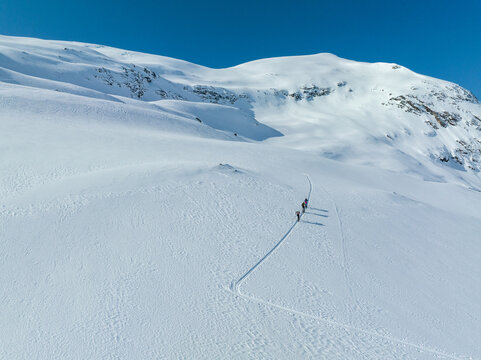 Aerial view of ski tourers ascending the snowy slopes of Hogstolen mountain with tracks visible in the deep snow under a clear blue sky in Fjord, More og Romsdal, Norway.