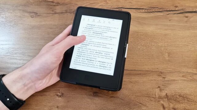 Modern digital reader device held above wooden table in casual setting