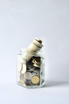 Glass jar filled with various coins and rolled dollar bills isolated on a white background with copy space.