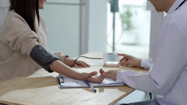 Close-up of a doctor measuring a female patient's blood pressure using a digital monitor at a clinic desk. Medical checkup, healthcare, and hypertension screening concept.