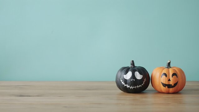 Two painted Halloween pumpkins on a wooden table against a light blue background.