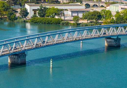 Aerial view of a steel truss road bridge spanning a wide river with cars, riverside industrial buildings and urban development in Le Pouzin, Auvergne-Rhone-Alpes, France.