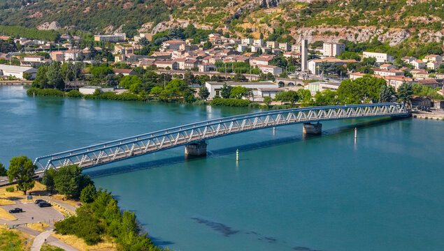 Aerial view of a steel truss road bridge crossing the Rhone river beside the town of Le Pouzin with industrial buildings and green hills in Le Pouzin, Auvergne-Rhone-Alpes, France.