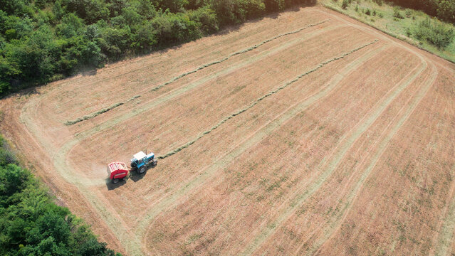 Tractor with a round baler collecting hay in an agricultural field. Rural landscape showing harvest activities