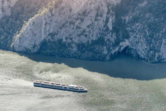 River cruise ship traveling through a deep canyon, with rugged cliffs and a cave entrance along the riverbank