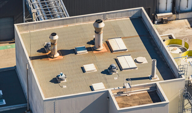 Aerial view of industrial rooftop ventilation systems, exhaust stacks, fans, and skylights on a production facility in Le Pouzin, Auvergne-Rhone-Alpes, France.