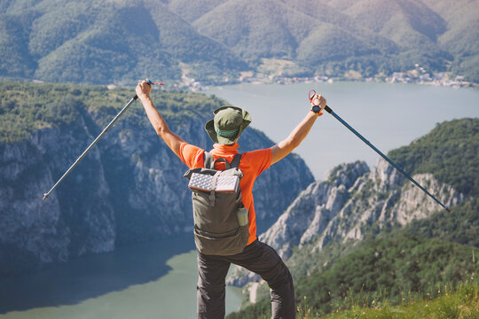 Hiker raising arms in triumph on a mountain peak overlooking a scenic Danube Iron Gates gorge and vast landscape, feeling freedom and success
