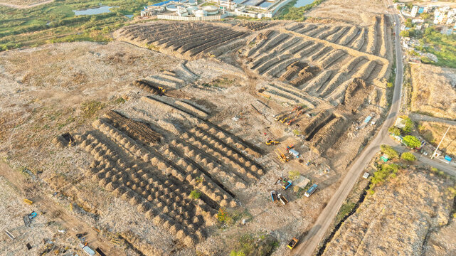Aerial view of a waste segregation and recycling facility with rows of mounds, heavy machinery, and industrial infrastructure in India.