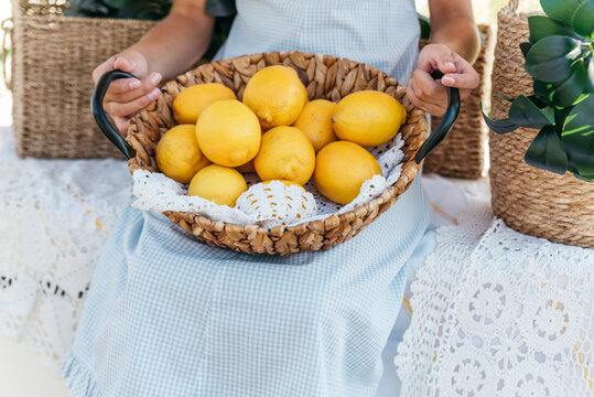 Smiling young girl Holding wicker basket filled with fresh lemons outdoors in a bright summer garden setting.