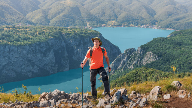 Hiker with backpack and trekking poles standing on a viewpoint, enjoying a panoramic view of the Danube Iron Gates river canyon in Djerdap park