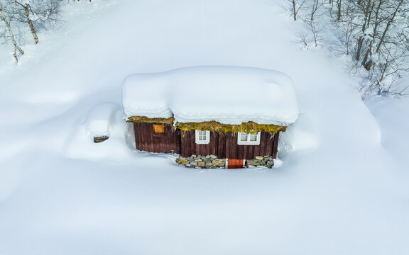 Aerial view of Jamtesetra, a traditional wooden cabin with a grass roof buried in deep snow, surrounded by a pristine winter landscape in Valldal, More og Romsdal, Norway.