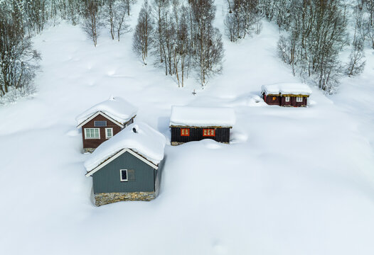 Aerial view of Jamtesetra with traditional wooden cabins partially buried in deep snow surrounded by a winter forest in Valldal, More og Romsdal, Norway.