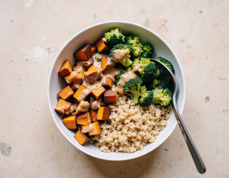 Healthy vegetarian buddha bowl with cooked quinoa, roasted pumpkin cubes, steamed broccoli, and creamy peanut dressing