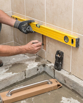Contractor marking stud locations on a tiled shower wall before installing a grab bar