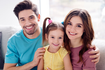 Obraz premium Happy young family smiling together at home with parents and daughter cuddling on couch and looking at camera