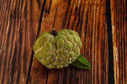 Green custard apple on rustic wooden surface with single leaf