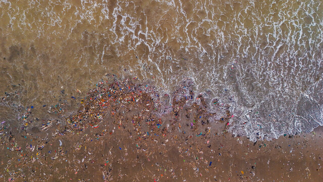 Aerial view of plastic waste and debris washed up on the sandy beach by ocean waves in Indonesia.