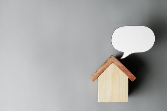 Wooden house model with blank speech bubble on gray background with copy space. Concept of real estate consultation, home loan advice, property message, and customer feedback.