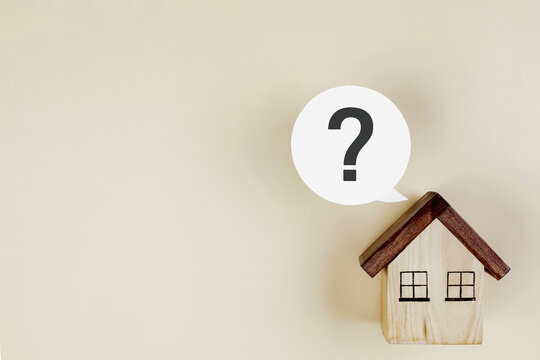 Small wooden house model with question mark speech bubble on cream background with copy space. Concept of real estate questions, home loan decision, house buying advice, and property search.