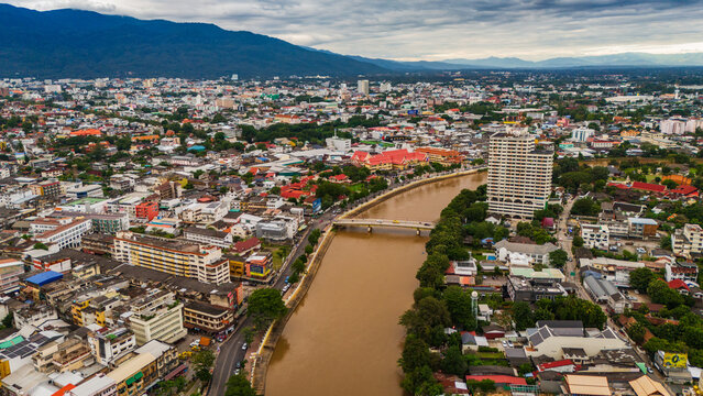 Aerial view of the Ping River flowing through the dense urban landscape with bridges, buildings, and lush greenery Chiang Mai, Thailand.