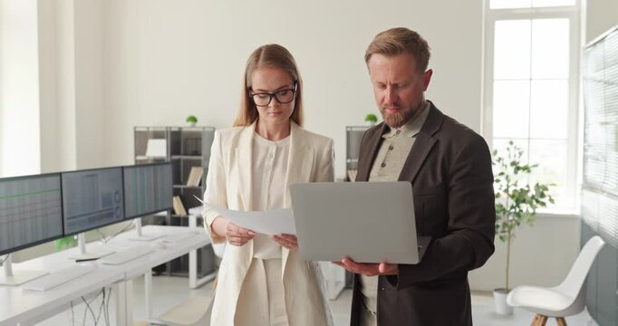 Businesswoman businessman evaluate paperwork on laptop. At an office meeting, coworkers discuss finance, accounting and collaboration, review figures. Clear teamwork and finance concept.