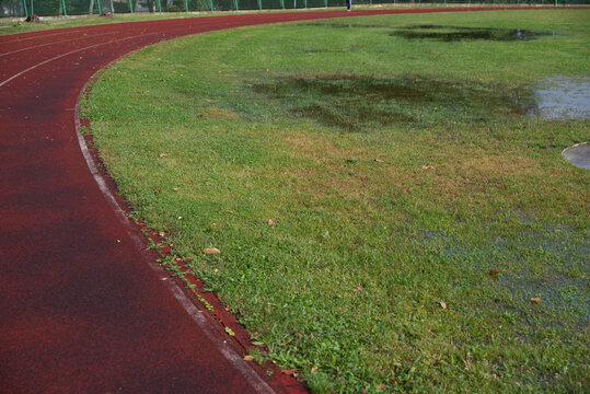Athletics track after heavy rain with flooded grass, making outdoor training difficult in autumn