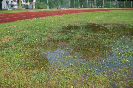 Athletics track after heavy rain with flooded grass, making outdoor training difficult in autumn
