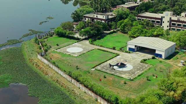 Aerial view of a helicopter parked on a private helipad near a lake and hangar facility in India.