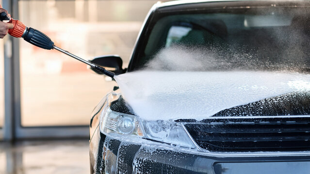 Pressure washer nozzle spraying foam with blurred car wash background banner.