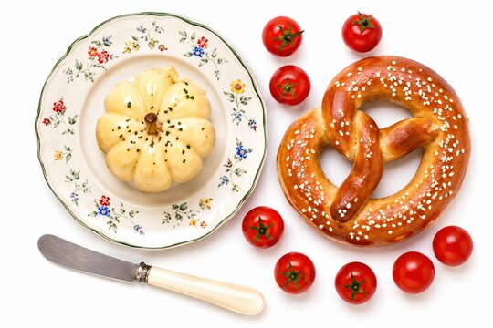 Fresh pretzel with small pumpkin and red tomatoes on a floral plate