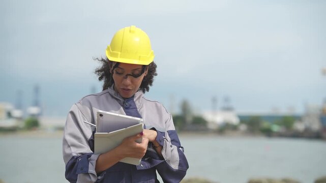 Female port engineer checking work documents and communicating by walkie talkie, shipping operation, maritime logistics, cargo ship inspection, seaport communication.