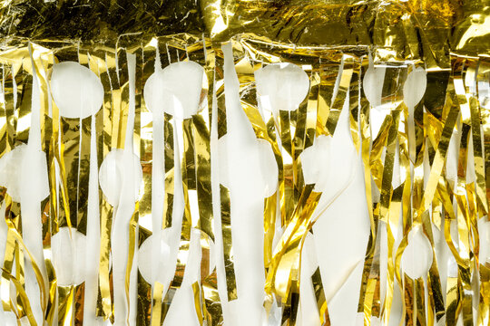 Festive background featuring shiny gold metallic foil tinsel streamers. Holiday or celebration background
