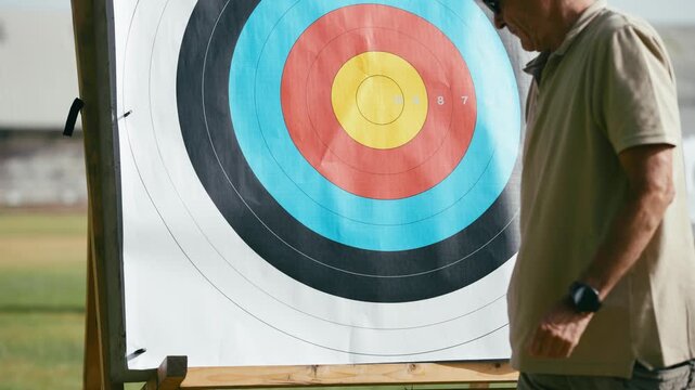 Elderly man setting up a paper target on a wooden stand for an archery competition. Active retirement and hobby for a senior citizen