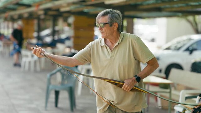 Focused senior man with glasses carefully attaching the string to his traditional wooden longbow, preparing for an archery practice session