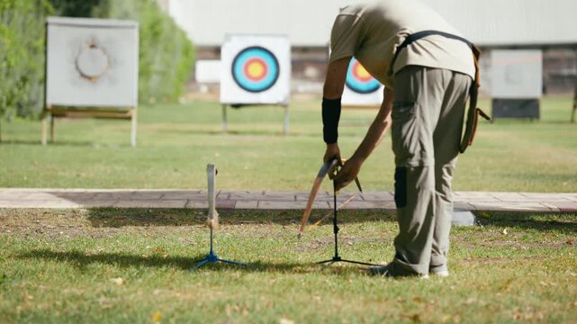 Experienced senior man finishing his archery practice and placing the recurve bow on a stand before leaving the grassy shooting range