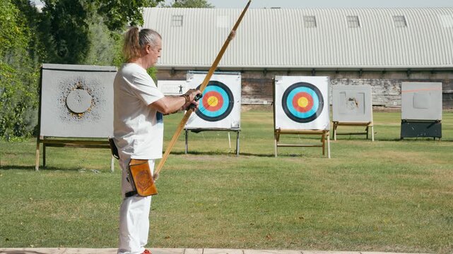 Senior male archer practicing his aim with a traditional wooden bow at an outdoor shooting range. Man focusing on the target with skill