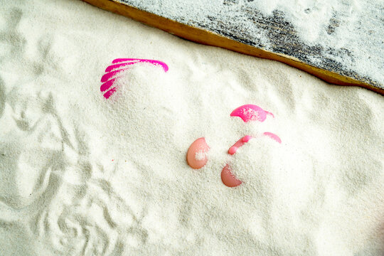 Partially buried pink plastic toys in clean white sand, viewed from above next to a wooden edge. Summer, natural or vacation background