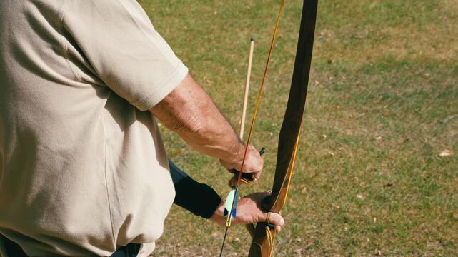 Archer carefully nocking an arrow on a longbow, then aiming and shooting. An older man practicing precision in an outdoor competition