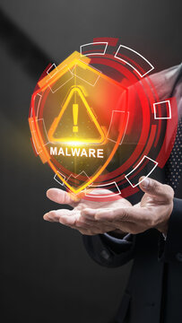 Businessman displaying a glowing orange holographic shield with a malware warning alert, representing cybersecurity threats and data defense. Cybersecurity concept
