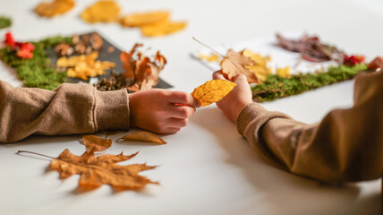 Naklejka premium Children's hands creating autumn nature crafts with leaves and moss