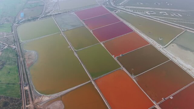 Aerial view of rectangular salt evaporation ponds displaying vibrant red, orange, yellow, and green hues at Sambhar Salt Lake in Rajasthan, India. The geometric grid pattern and colours stand out.