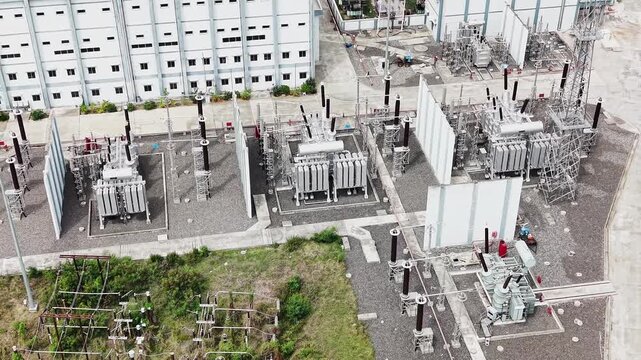Aerial view of an electric substation featuring high voltage transformers and industrial equipment set within a fenced facility in India.